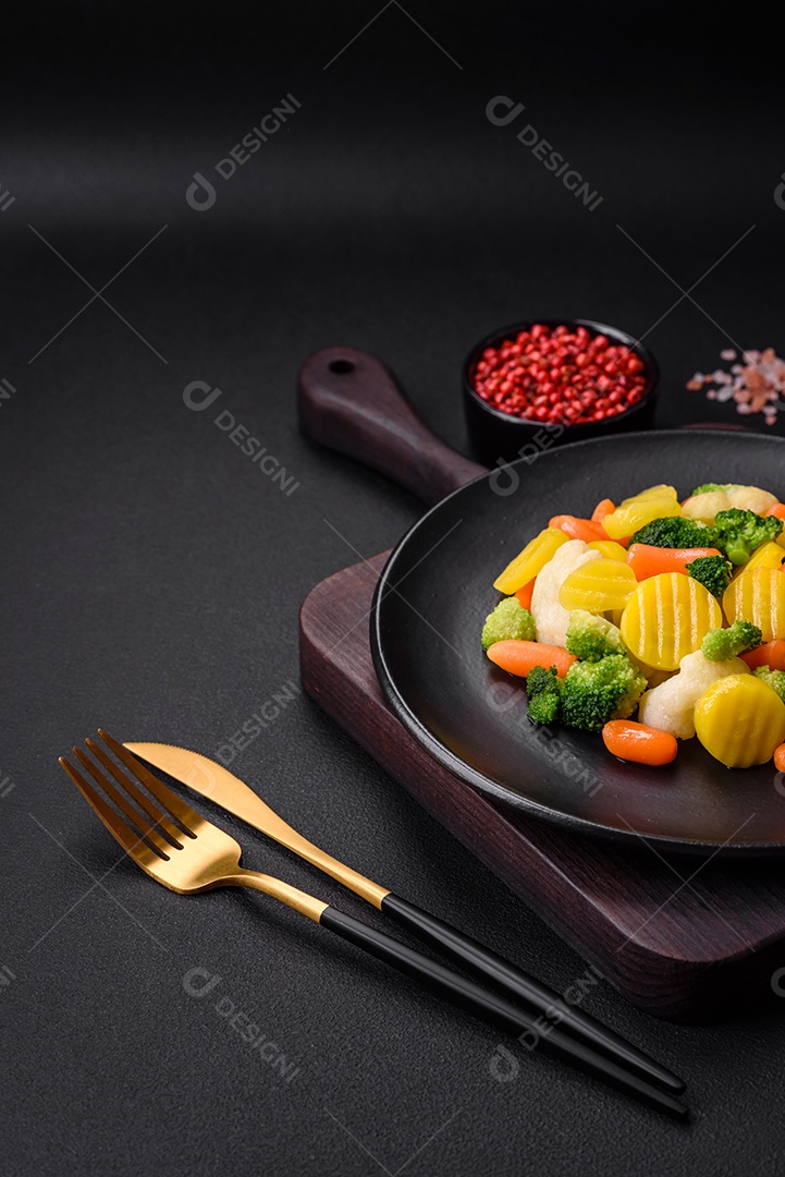 Deliciosos legumes frescos cozidos cenouras, brócolis, couve-flor em uma placa preta sobre um fundo escuro de concreto