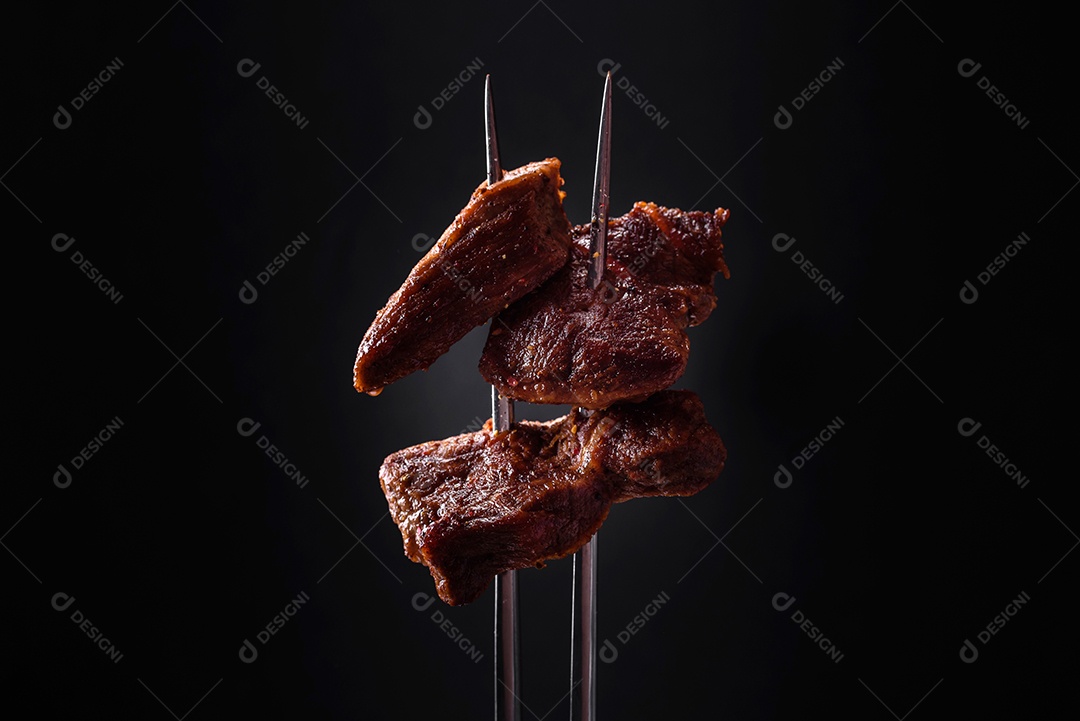 Vários pedaços de carne fresca grelhada com especiarias e ervas e amarrados num garfo sobre um fundo escuro de concreto