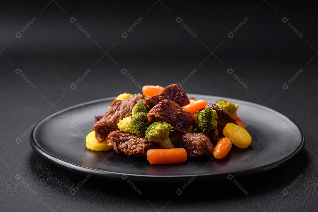 Deliciosas cenouras frescas de carne e legumes, brócolis, couve-flor em uma placa preta sobre um fundo escuro de concreto