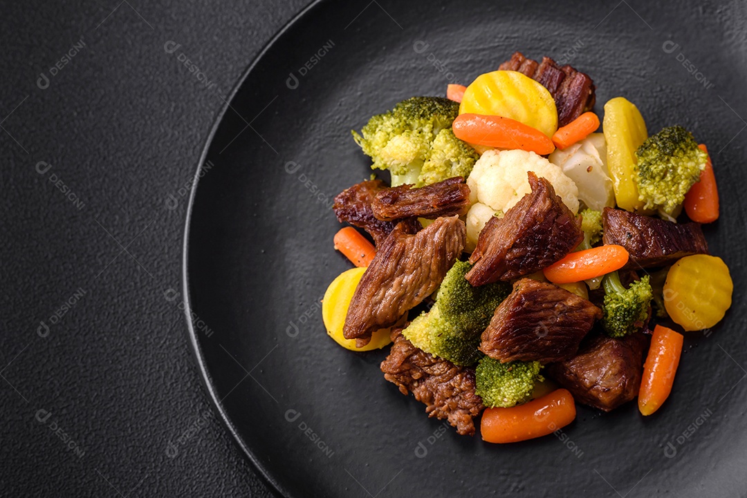 Deliciosas cenouras frescas de carne e legumes, brócolis, couve-flor em uma placa preta sobre um fundo escuro de concreto