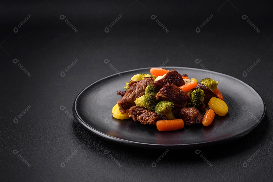 Deliciosas cenouras frescas de carne e legumes, brócolis, couve-flor em uma placa preta sobre um fundo escuro de concreto