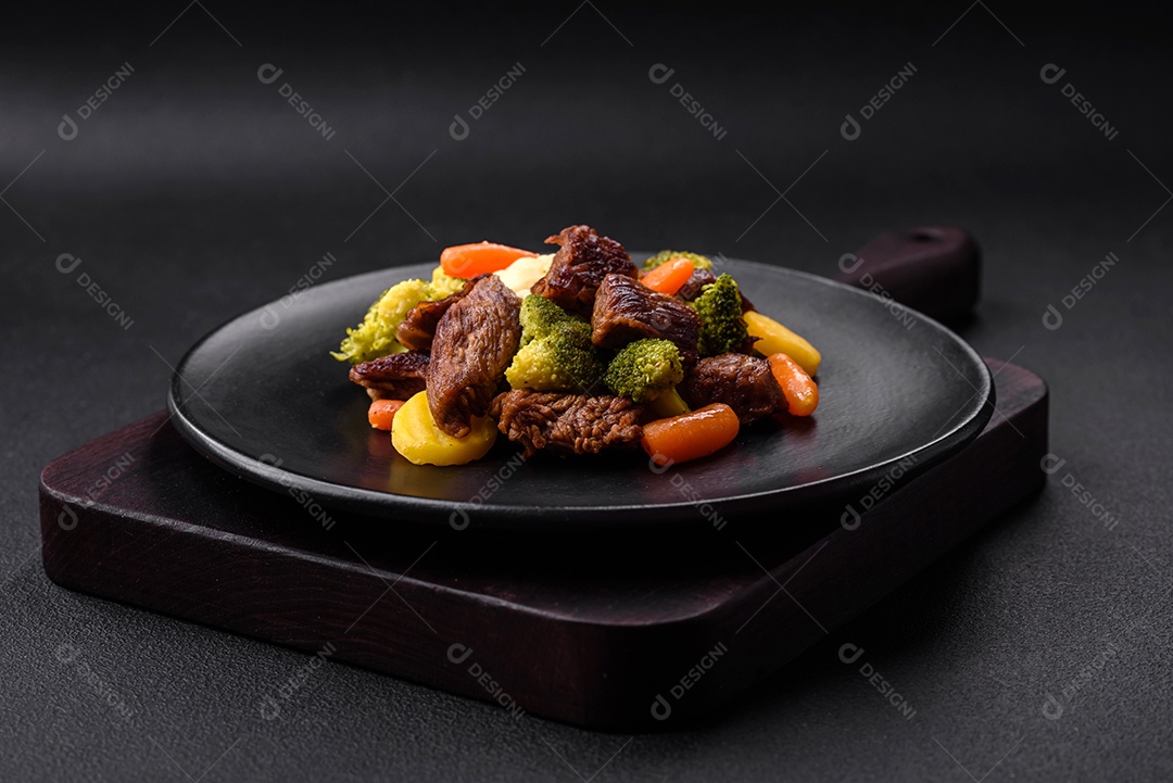 Deliciosas cenouras frescas de carne e legumes, brócolis, couve-flor em uma placa preta sobre um fundo escuro de concreto