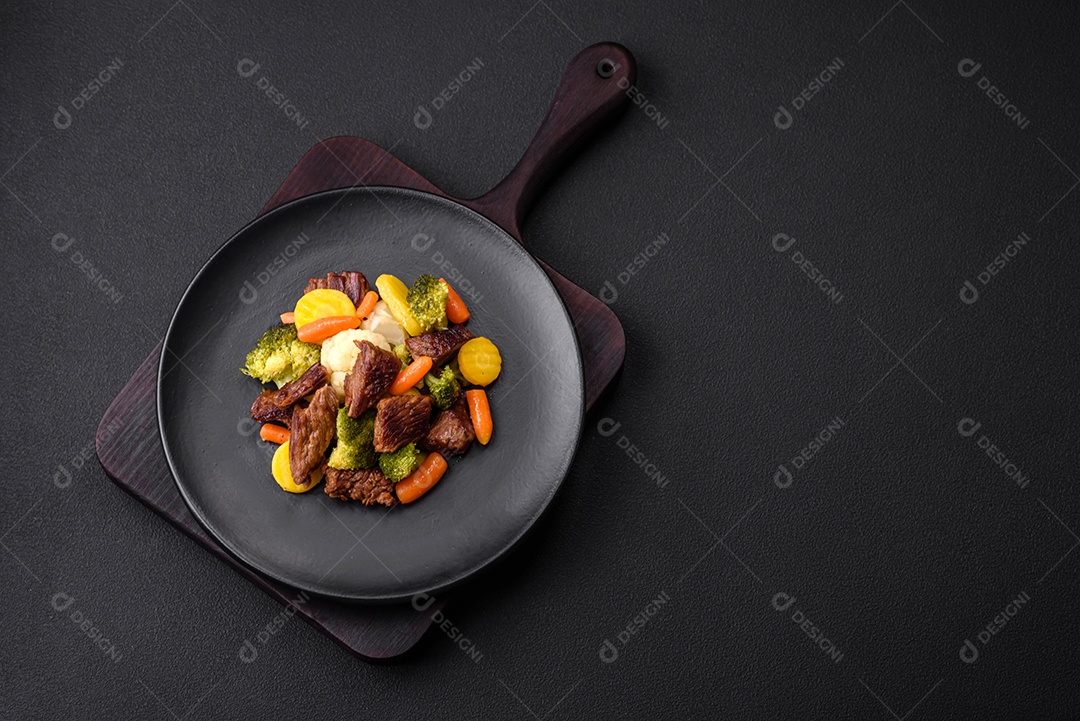 Deliciosas cenouras frescas de carne e legumes, brócolis, couve-flor em uma placa preta sobre um fundo escuro de concreto