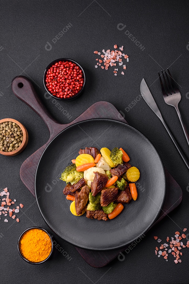 Deliciosas cenouras frescas de carne e legumes, brócolis, couve-flor em uma placa preta sobre um fundo escuro de concreto