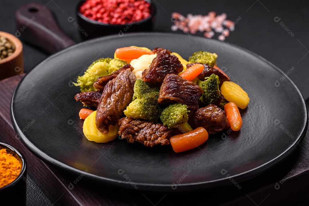 Deliciosas cenouras frescas de carne e legumes, brócolis, couve-flor em uma placa preta sobre um fundo escuro de concreto