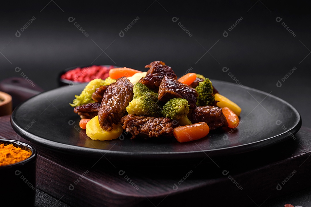 Deliciosas cenouras frescas de carne e legumes, brócolis, couve-flor em uma placa preta sobre um fundo escuro de concreto