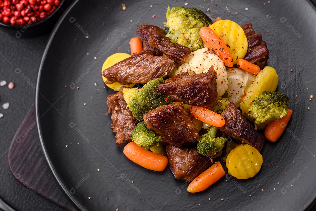 Deliciosas cenouras frescas de carne e legumes, brócolis, couve-flor em uma placa preta sobre um fundo escuro de concreto