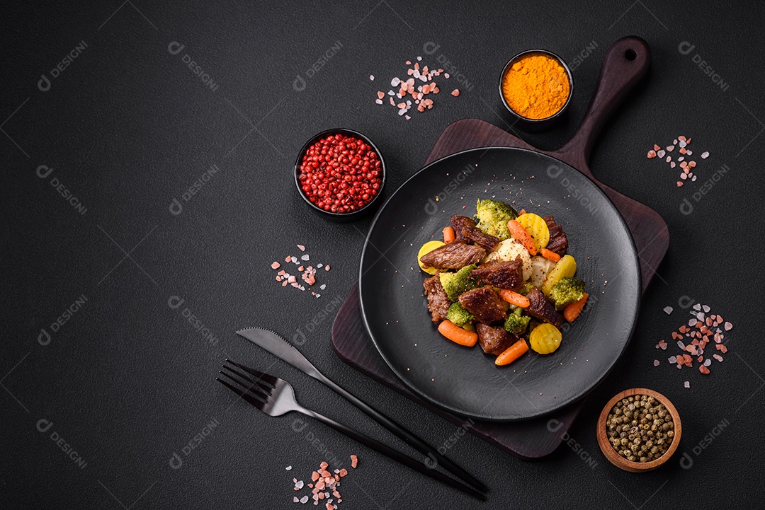 Deliciosas cenouras frescas de carne e legumes, brócolis, couve-flor em uma placa preta sobre um fundo escuro de concreto