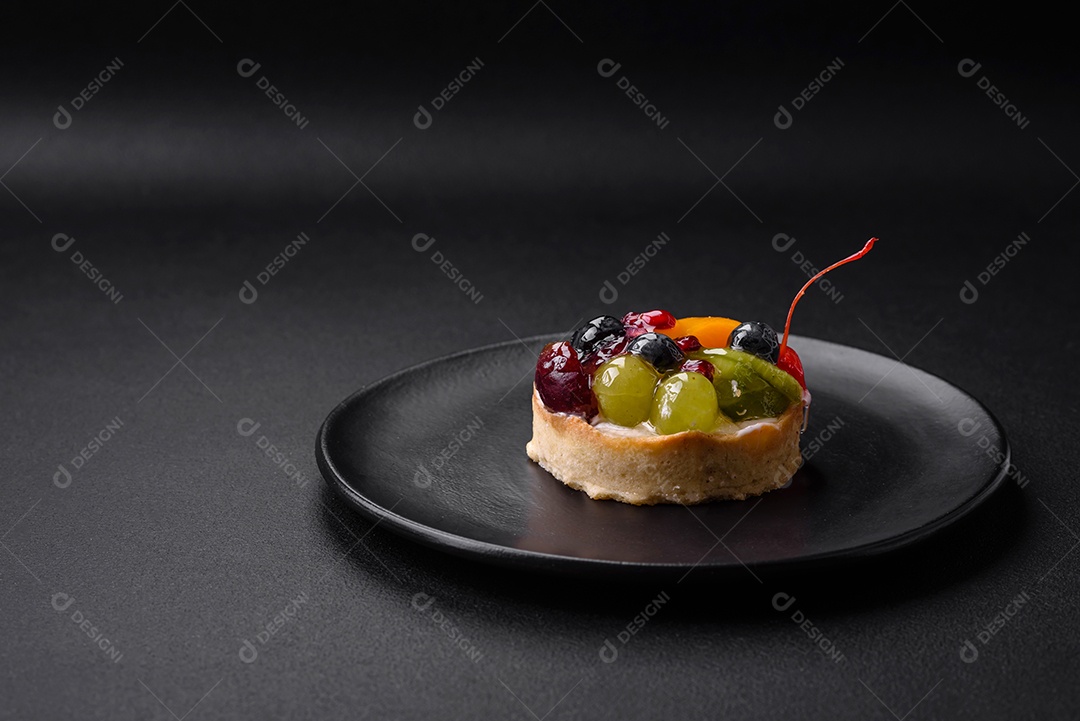 Deliciosa torta fresca com mirtilos, cerejas, uvas em uma placa de cerâmica preta sobre um fundo escuro de concreto