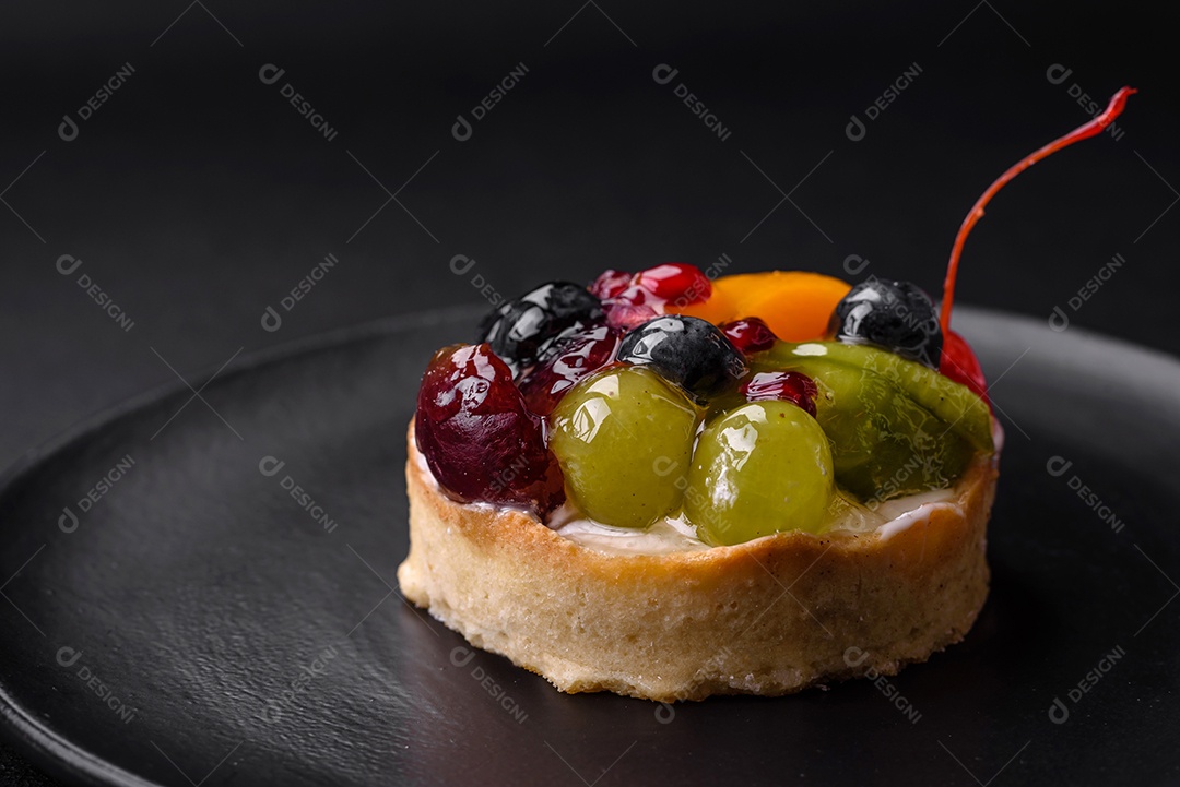Deliciosa torta fresca com mirtilos, cerejas, uvas em uma placa de cerâmica preta sobre um fundo escuro de concreto