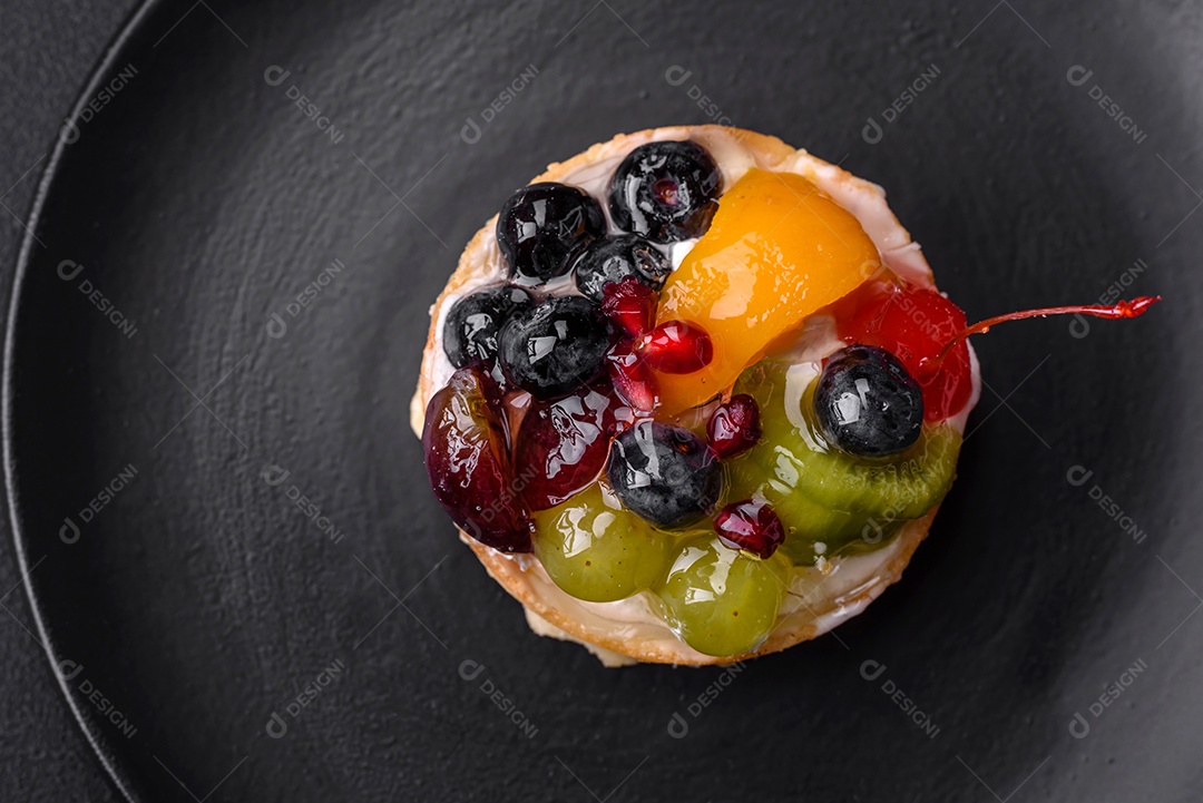 Deliciosa torta fresca com mirtilos, cerejas, uvas em uma placa de cerâmica preta sobre um fundo escuro de concreto
