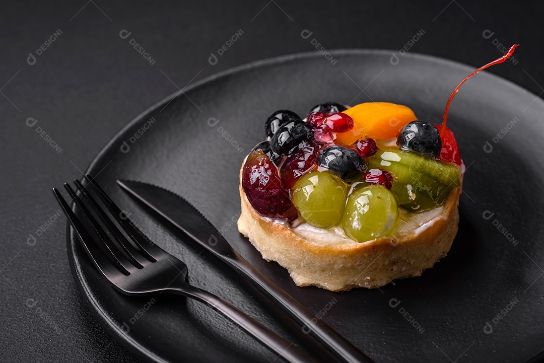 Deliciosa torta fresca com mirtilos, cerejas, uvas em uma placa de cerâmica preta sobre um fundo escuro de concreto