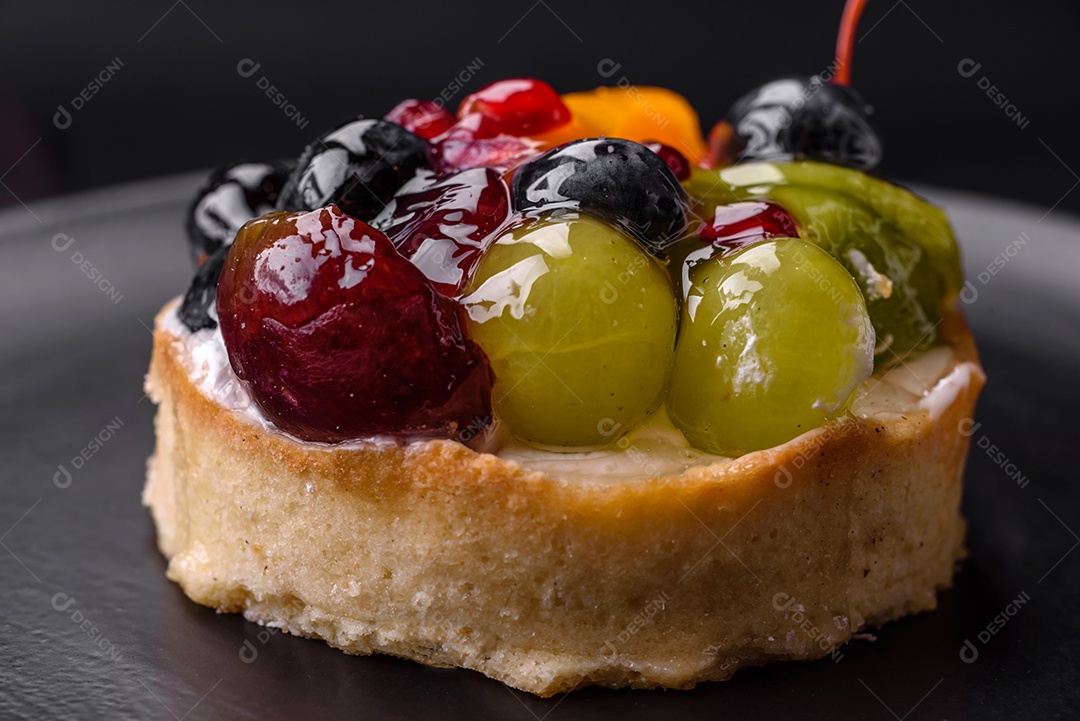 Deliciosa torta fresca com mirtilos, cerejas, uvas em uma placa de cerâmica preta sobre um fundo escuro de concreto