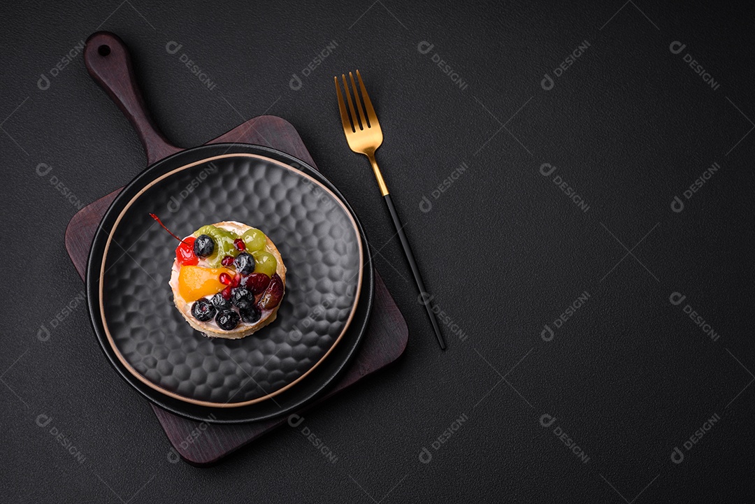 Deliciosa torta fresca com mirtilos, cerejas, uvas em uma placa de cerâmica preta sobre um fundo escuro de concreto