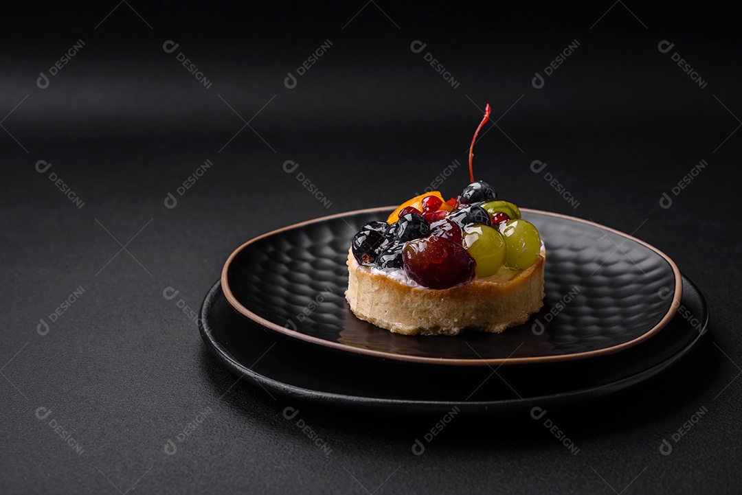 Deliciosa torta fresca com mirtilos, cerejas, uvas em uma placa de cerâmica preta sobre um fundo escuro de concreto