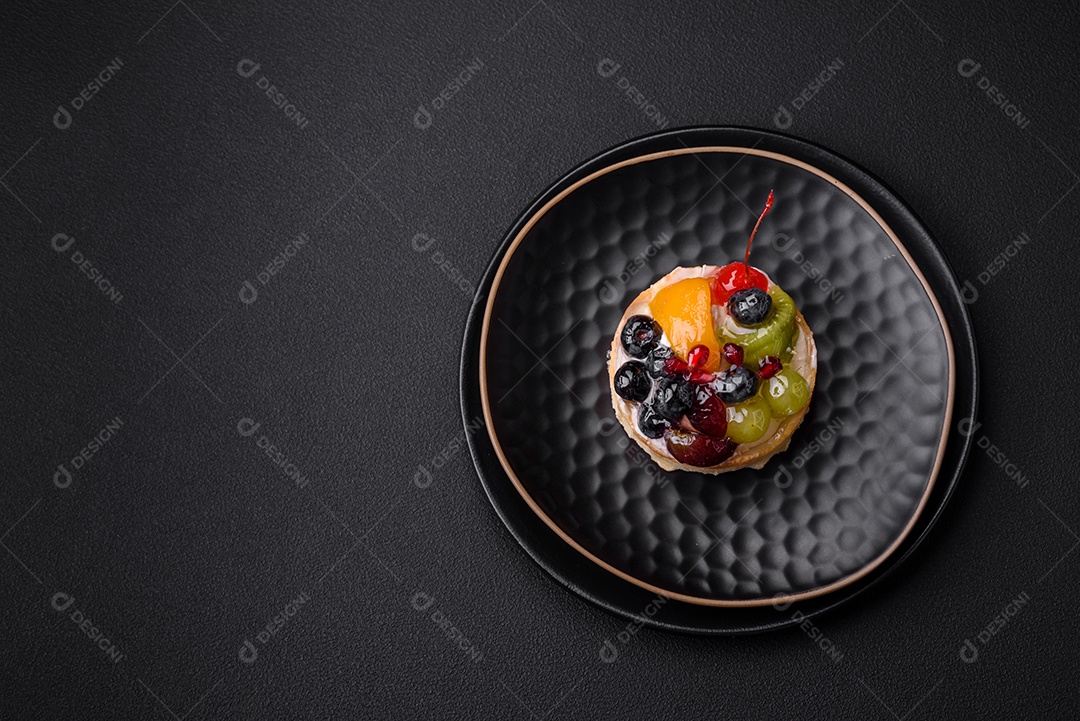 Deliciosa torta fresca com mirtilos, cerejas, uvas em uma placa de cerâmica preta sobre um fundo escuro de concreto