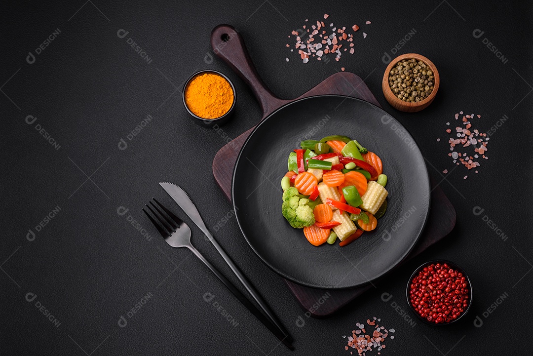 Deliciosos vegetais suculentos de brócolis, cenouras, feijões de espargos, pimentões cozinhados em uma placa preta sobre um fundo escuro de concreto