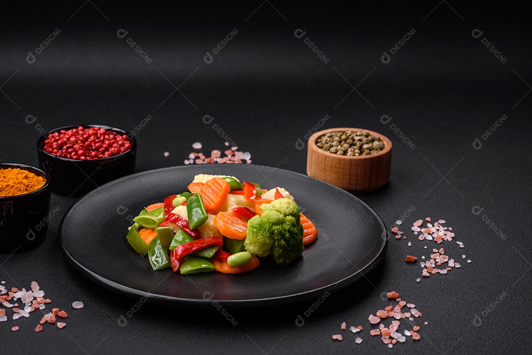Deliciosos vegetais suculentos de brócolis, cenouras, feijões de espargos, pimentões cozinhados em uma placa preta sobre um fundo escuro de concreto