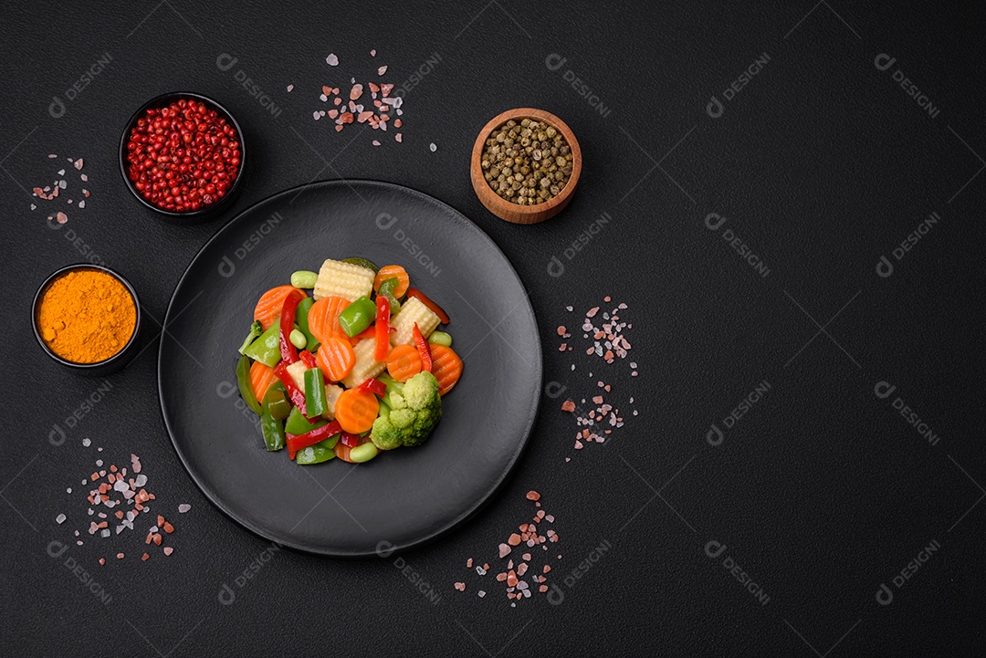 Deliciosos vegetais suculentos de brócolis, cenouras, feijões de espargos, pimentões cozinhados em uma placa preta sobre um fundo escuro de concreto