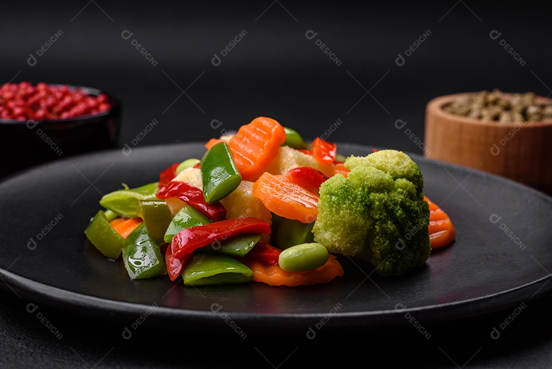 Deliciosos vegetais suculentos de brócolis, cenouras, feijões de espargos, pimentões cozinhados em uma placa preta sobre um fundo escuro de concreto