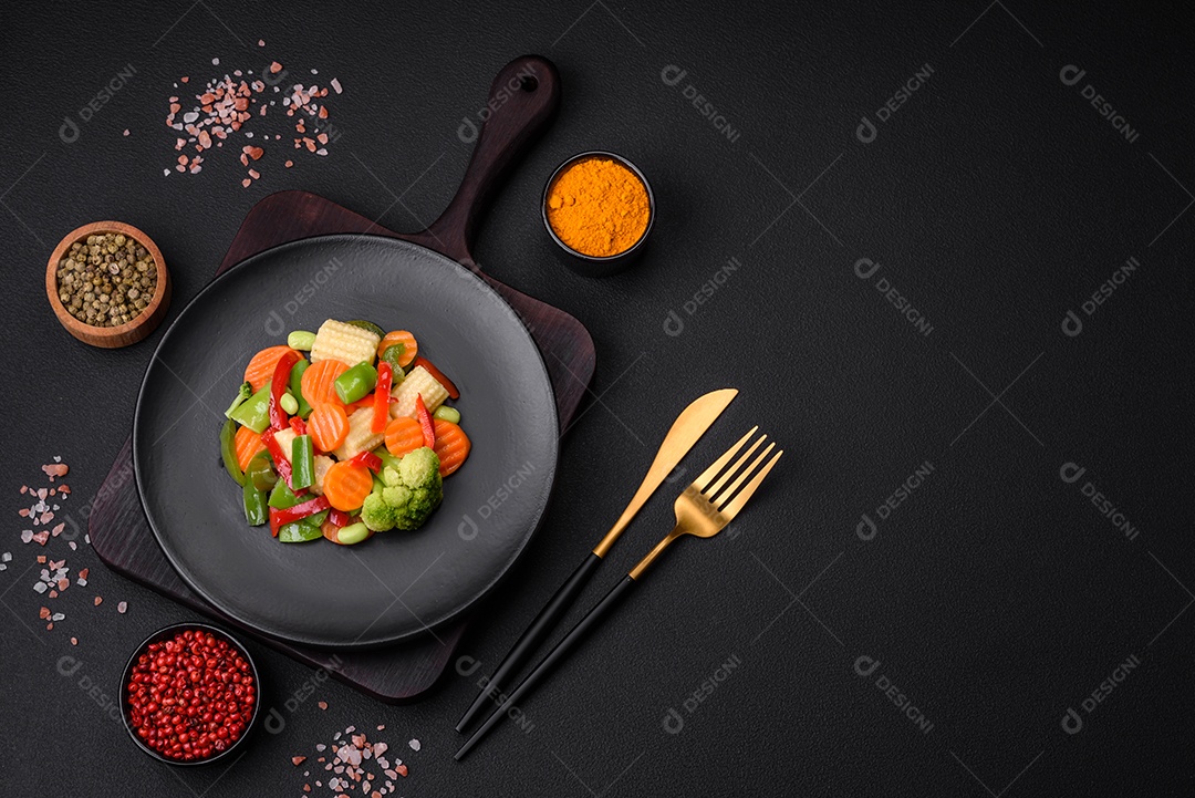 Deliciosos vegetais suculentos de brócolis, cenouras, feijões de espargos, pimentões cozinhados em uma placa preta sobre um fundo escuro de concreto