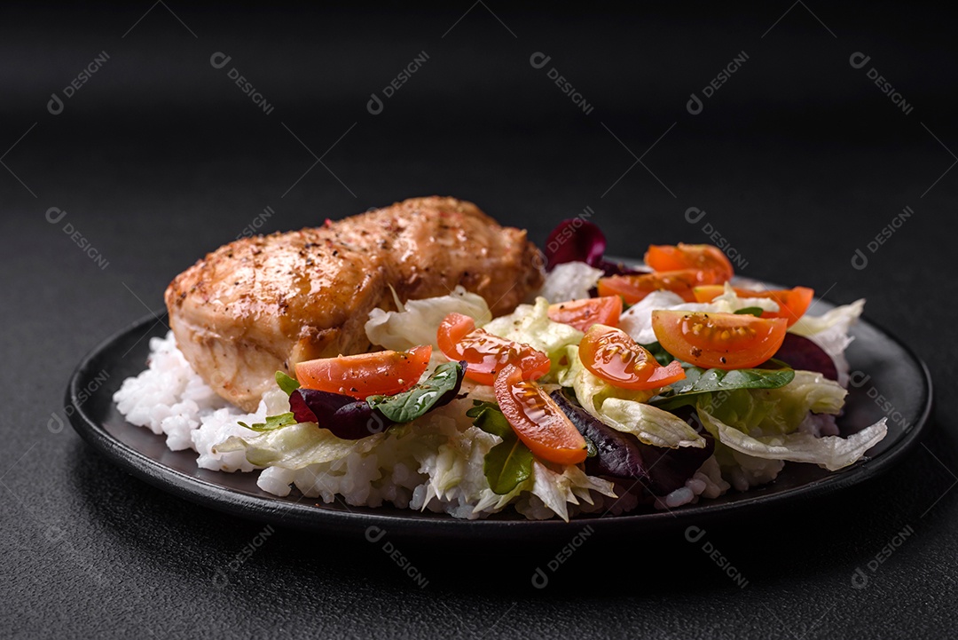 Delicioso café da manhã saudável composto por frango, arroz, verduras e tomate cereja em uma placa de cerâmica preta sobre um fundo escuro de concreto