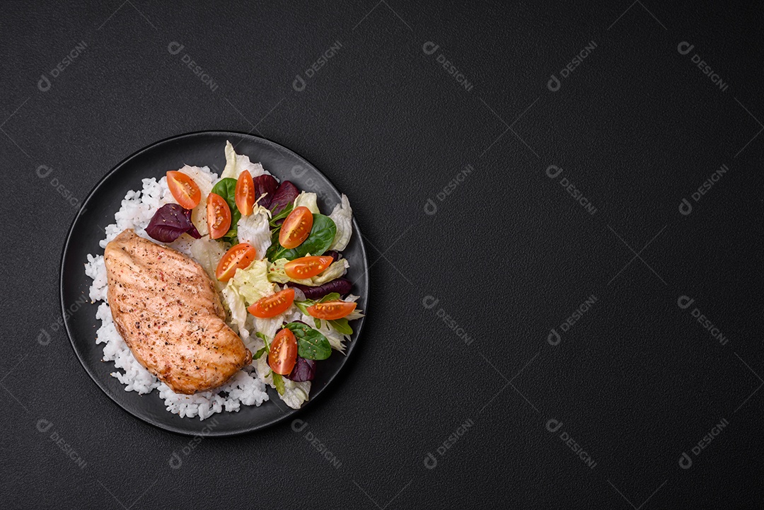 Delicioso café da manhã saudável composto por frango, arroz, verduras e tomate cereja em uma placa de cerâmica preta sobre um fundo escuro de concreto