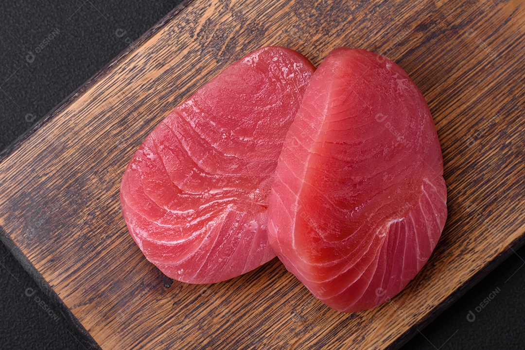 Duas fatias frescas de filé de atum cru com especiarias e ervas sobre um fundo escuro de concreto
