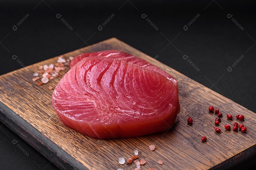 Duas fatias frescas de filé de atum cru com especiarias e ervas sobre um fundo escuro de concreto