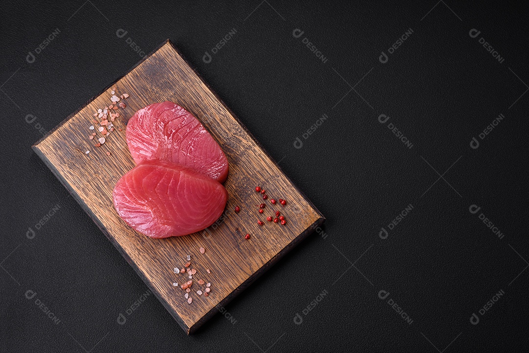 Duas fatias frescas de filé de atum cru com especiarias e ervas sobre um fundo escuro de concreto