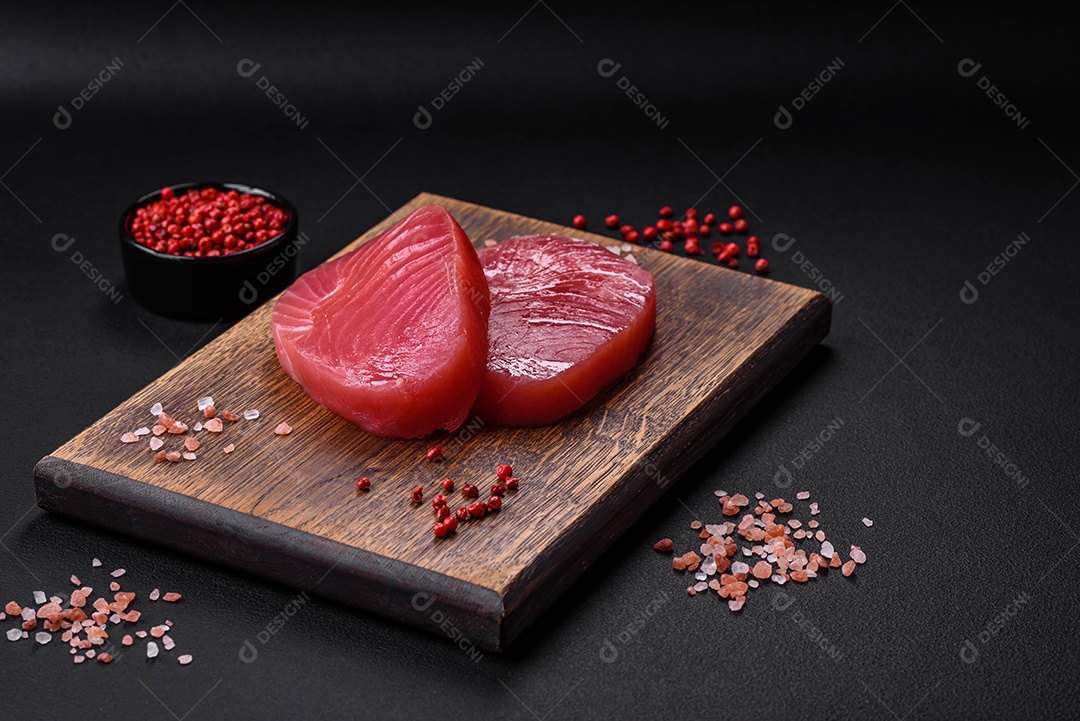 Duas fatias frescas de filé de atum cru com especiarias e ervas sobre um fundo escuro de concreto