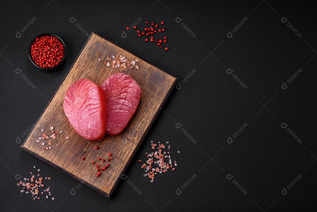 Duas fatias frescas de filé de atum cru com especiarias e ervas sobre um fundo escuro de concreto