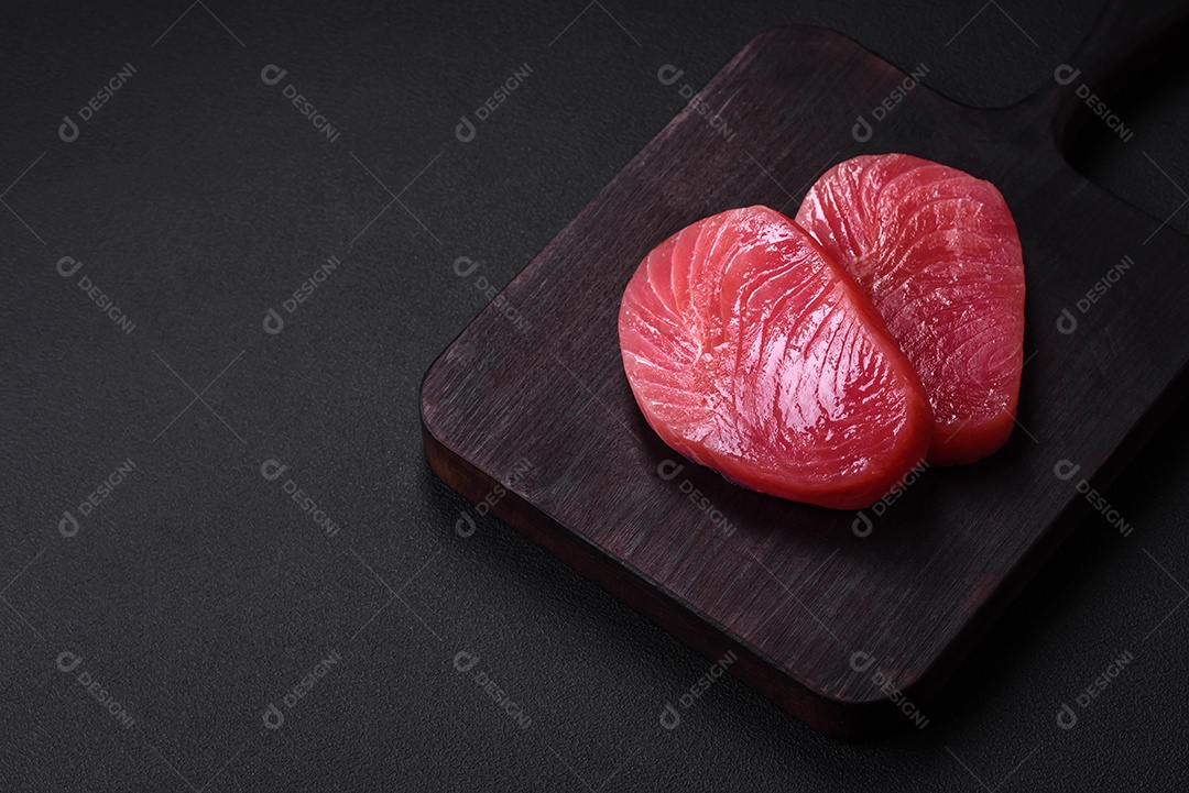 Duas fatias frescas de filé de atum cru com especiarias e ervas sobre um fundo escuro de concreto