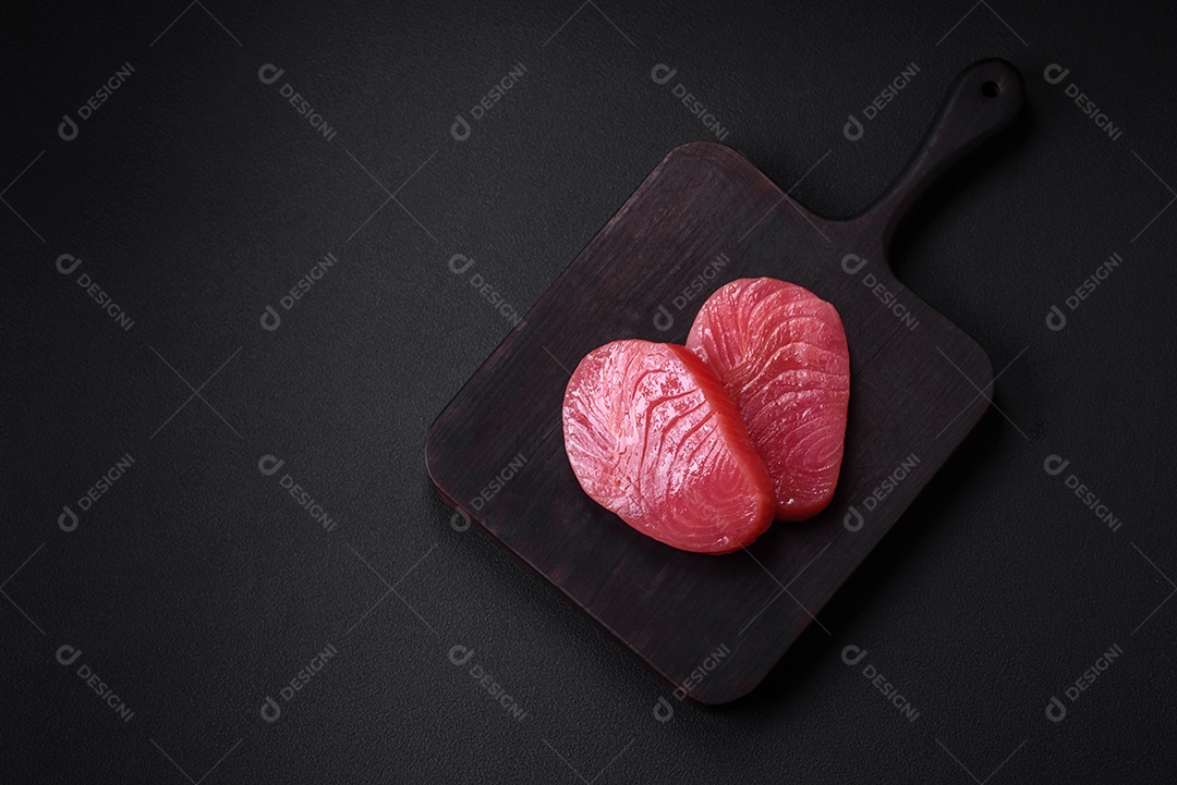 Duas fatias frescas de filé de atum cru com especiarias e ervas sobre um fundo escuro de concreto
