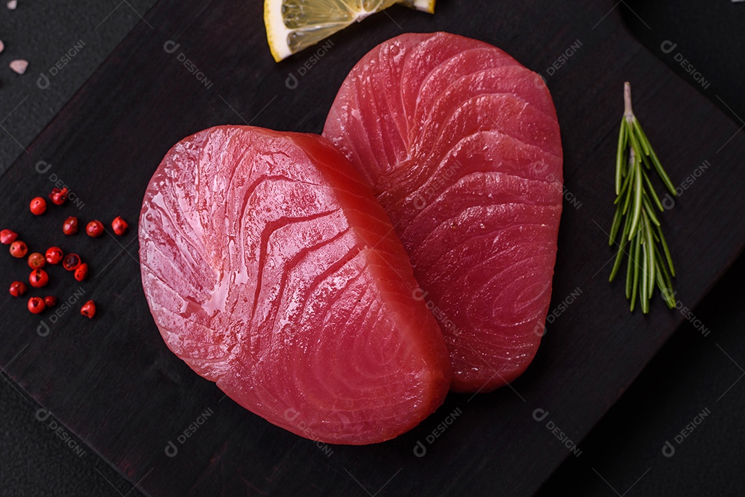 Duas fatias frescas de filé de atum cru com especiarias e ervas sobre um fundo escuro de concreto