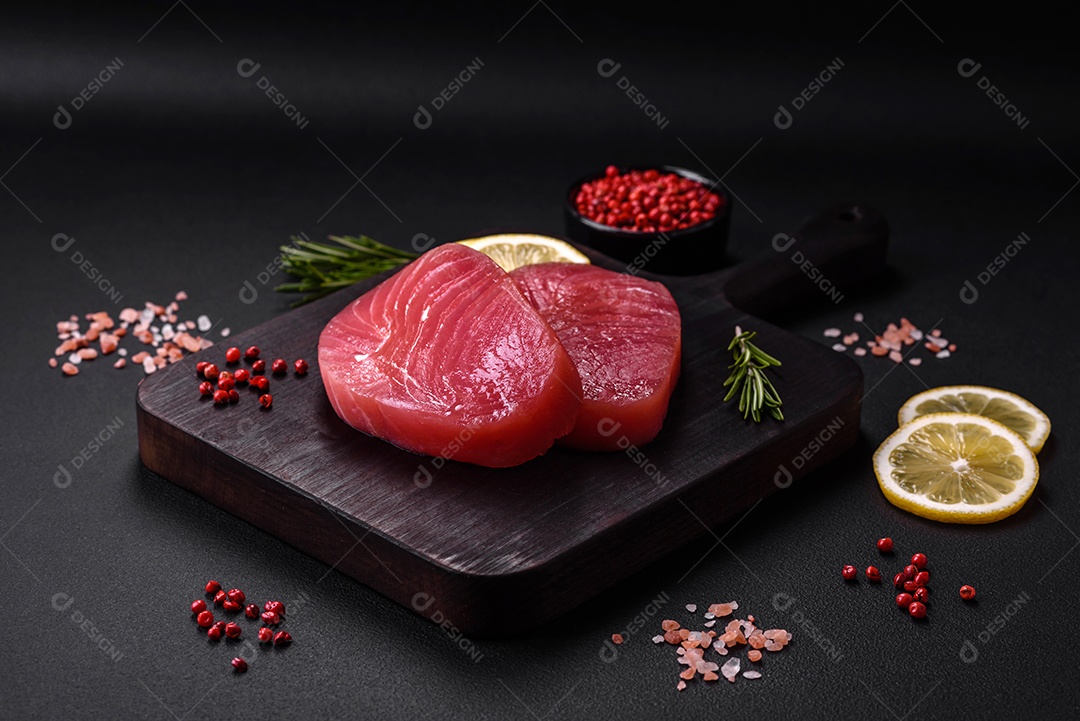 Duas fatias frescas de filé de atum cru com especiarias e ervas sobre um fundo escuro de concreto