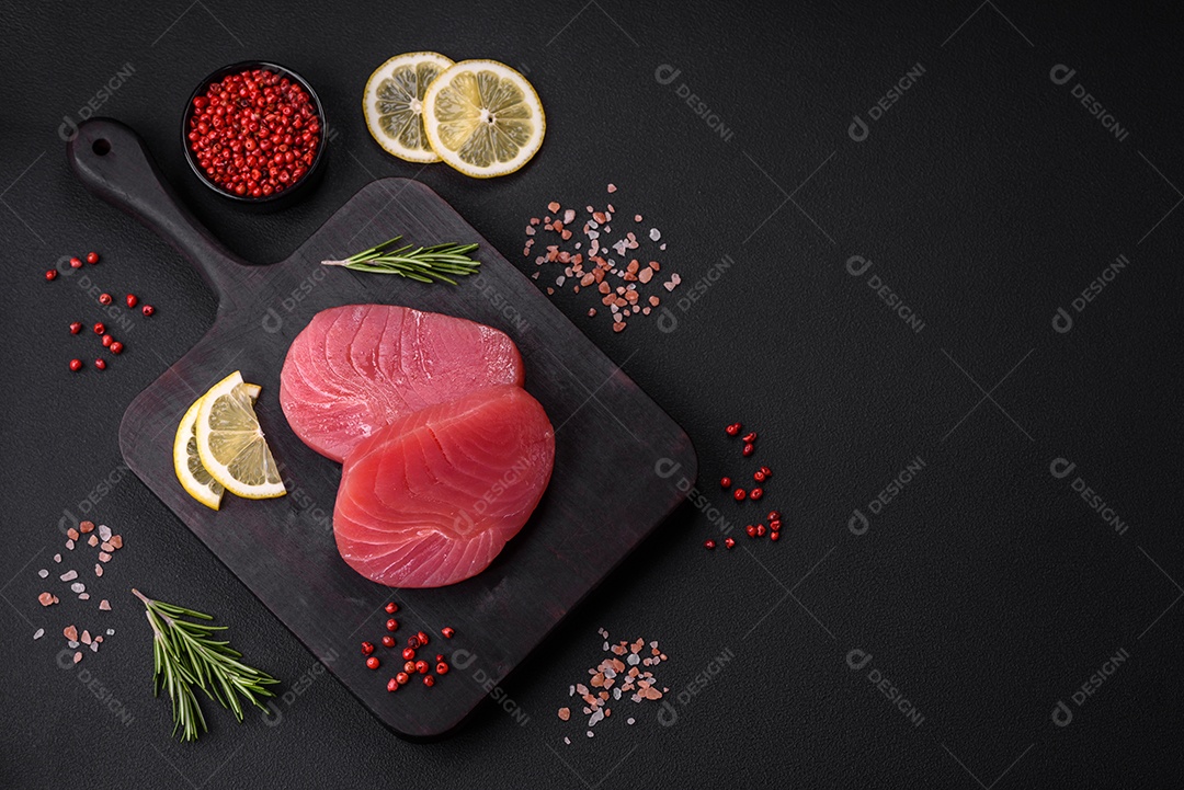 Duas fatias frescas de filé de atum cru com especiarias e ervas sobre um fundo escuro de concreto
