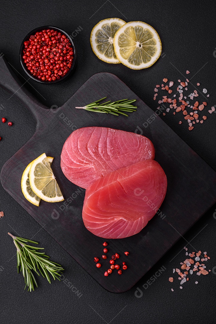 Duas fatias frescas de filé de atum cru com especiarias e ervas sobre um fundo escuro de concreto