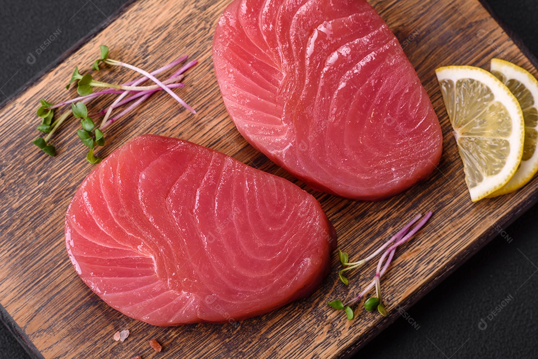 Duas fatias frescas de filé de atum cru com especiarias e ervas sobre um fundo escuro de concreto