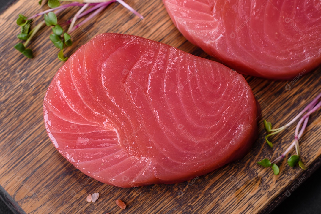 Duas fatias frescas de filé de atum cru com especiarias e ervas sobre um fundo escuro de concreto