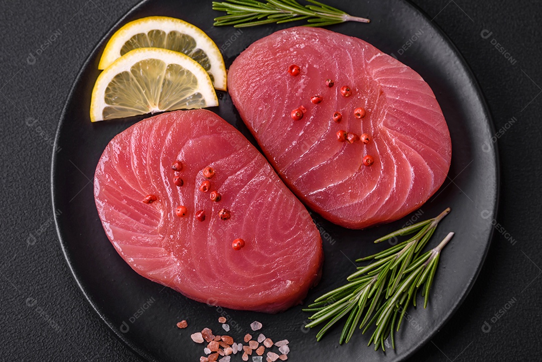 Duas fatias frescas de filé de atum cru com especiarias e ervas sobre um fundo escuro de concreto
