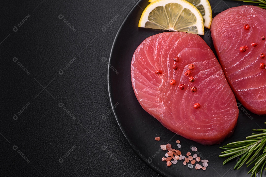 Duas fatias frescas de filé de atum cru com especiarias e ervas sobre um fundo escuro de concreto