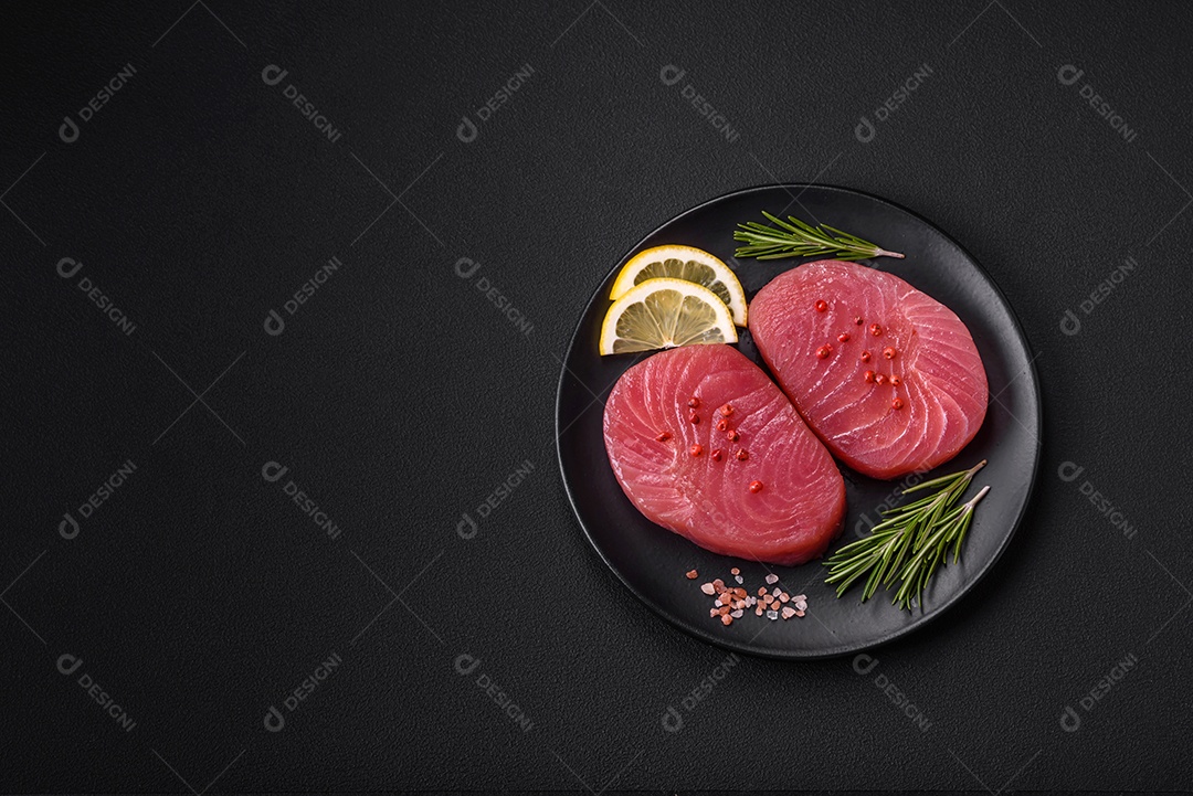 Duas fatias frescas de filé de atum cru com especiarias e ervas sobre um fundo escuro de concreto