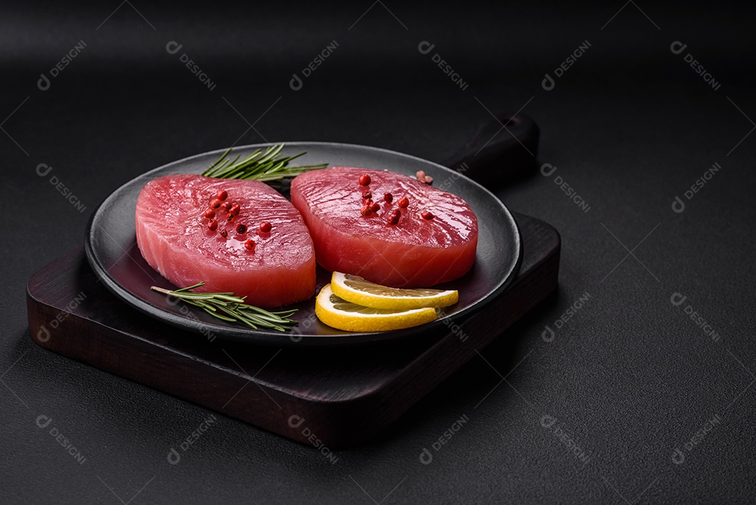Duas fatias frescas de filé de atum cru com especiarias e ervas sobre um fundo escuro de concreto