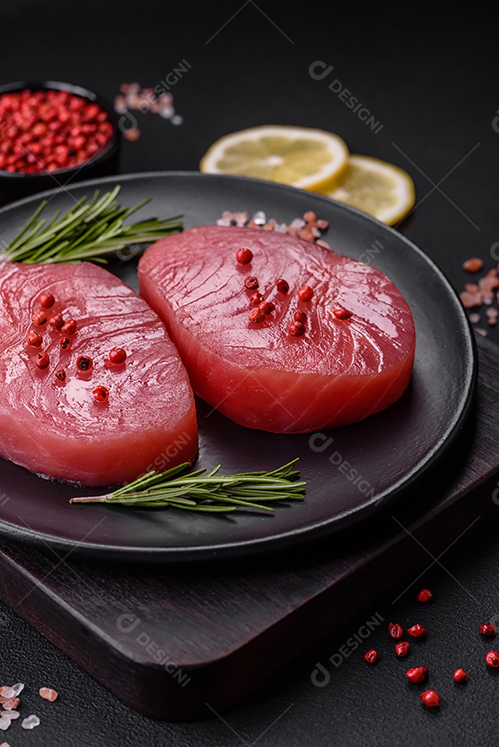 Duas fatias frescas de filé de atum cru com especiarias e ervas sobre um fundo escuro de concreto