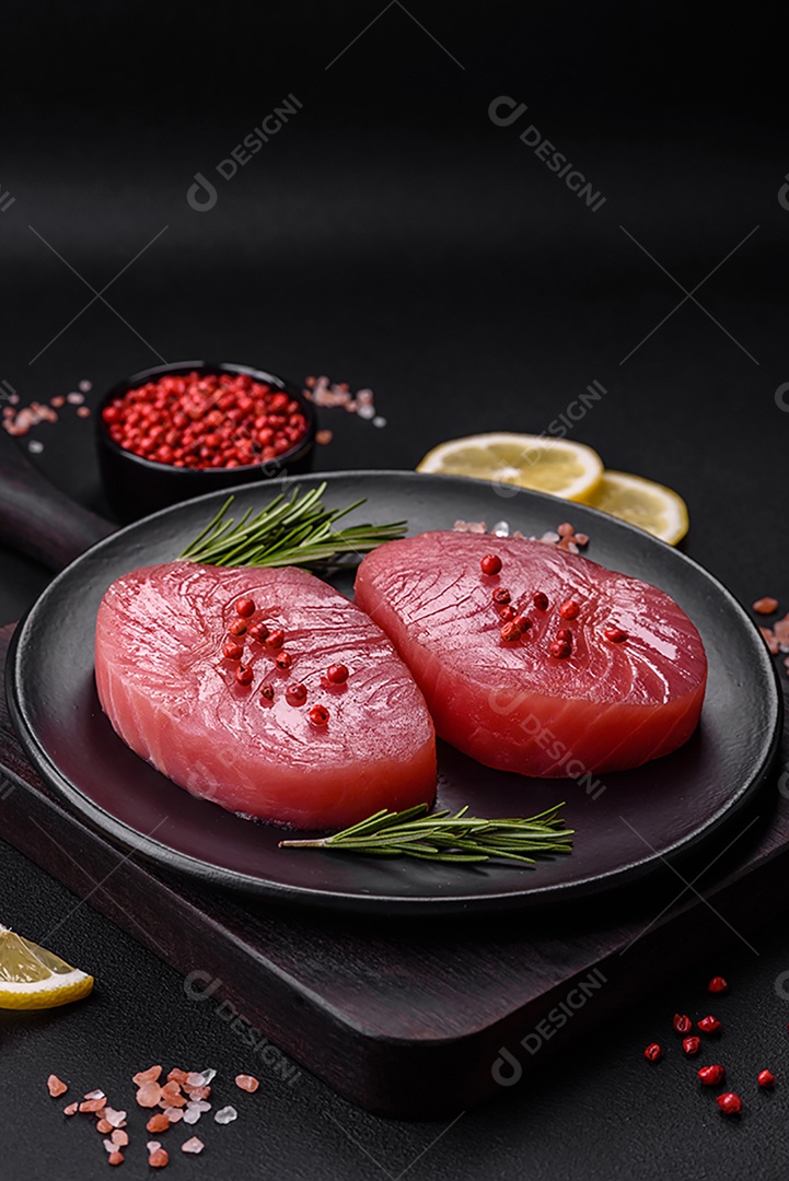 Duas fatias frescas de filé de atum cru com especiarias e ervas sobre um fundo escuro de concreto