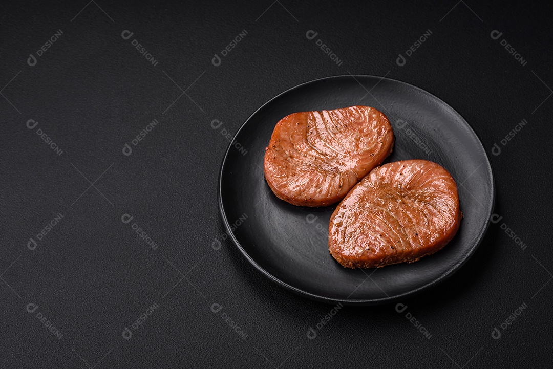 Duas fatias assadas de filé de atum com especiarias e ervas sobre um fundo escuro de concreto