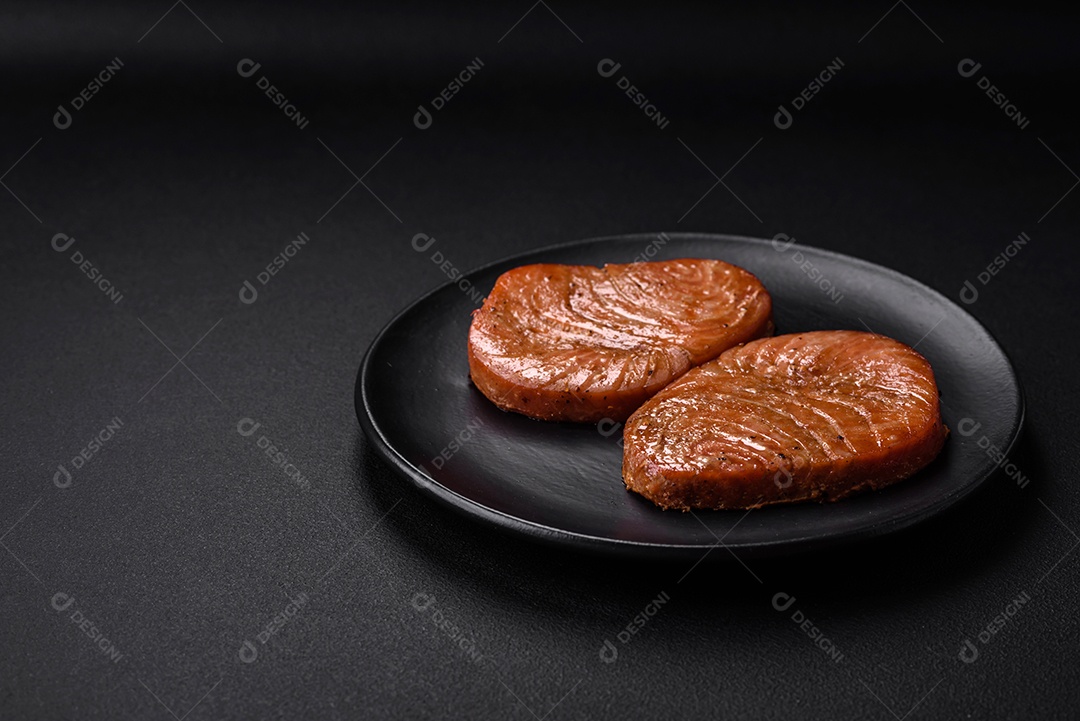 Duas fatias assadas de filé de atum com especiarias e ervas sobre um fundo escuro de concreto