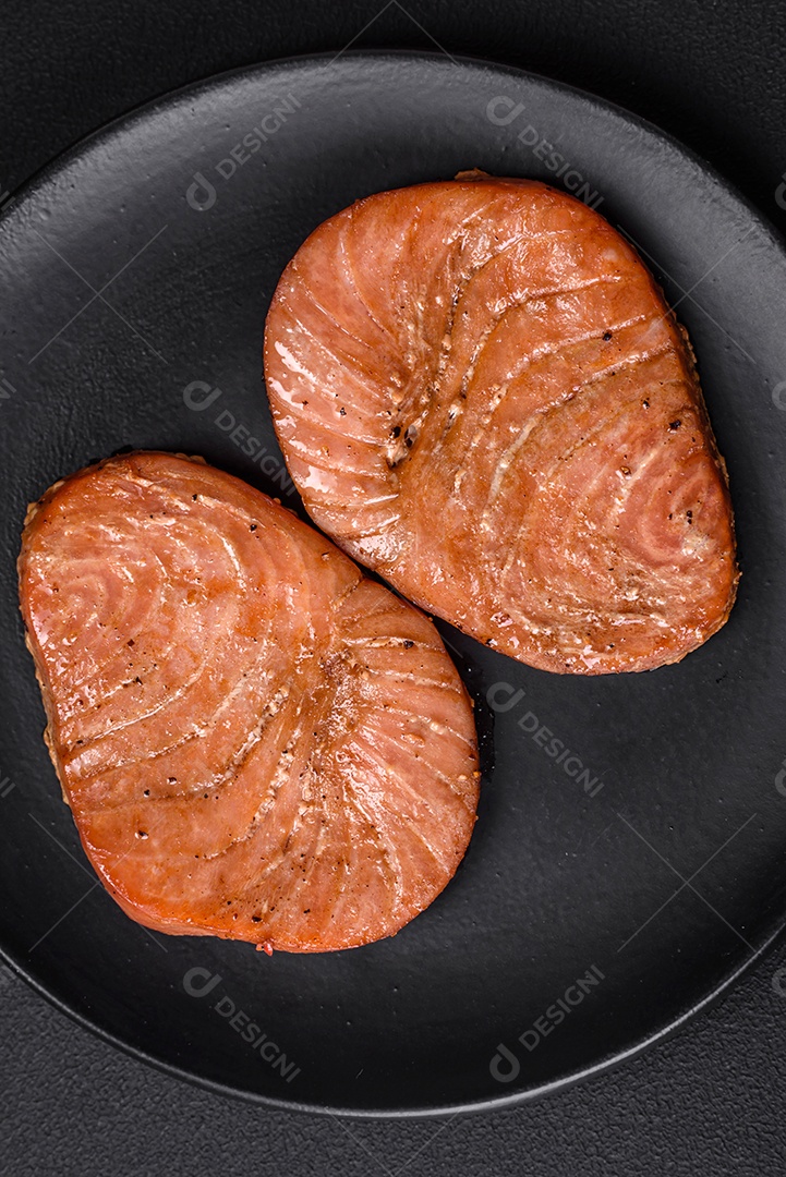 Duas fatias assadas de filé de atum com especiarias e ervas sobre um fundo escuro de concreto