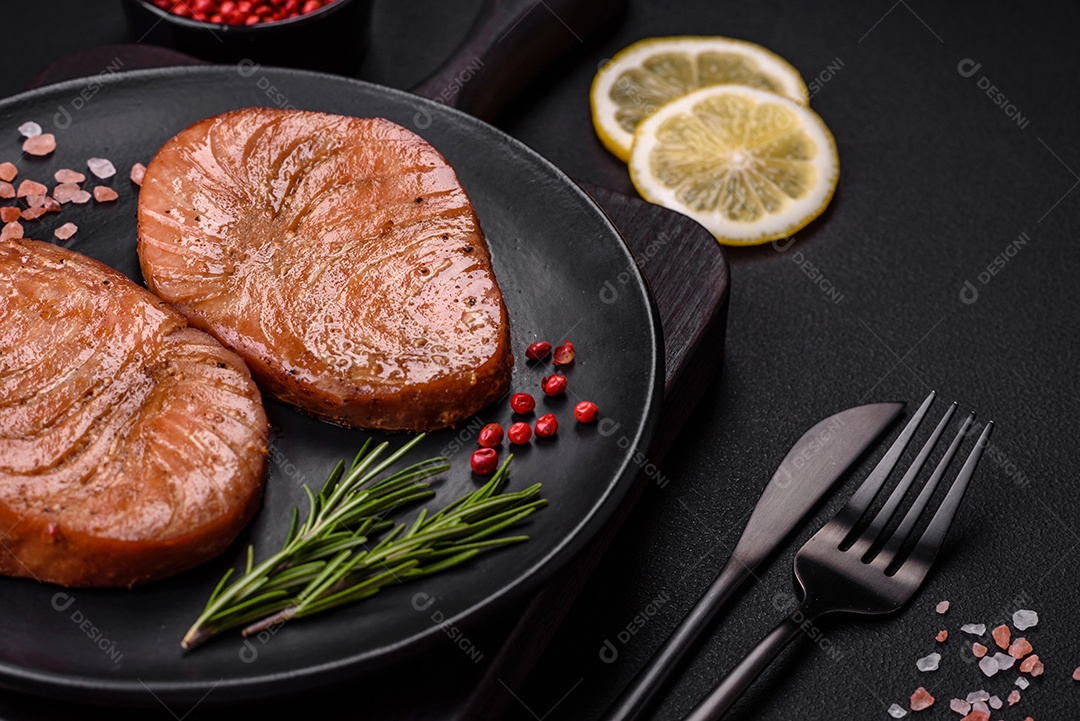 Duas fatias assadas de filé de atum com especiarias e ervas sobre um fundo escuro de concreto